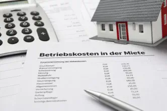 Dokument mit dem Titel „Betriebskosten in der Miete“ liegt auf einem Schreibtisch neben Taschenrechner, Stift und Modellhaus; aufgelistet sind typische Nebenkosten wie Wasser, Heizung und Müllabfuhr mit Eurobeträgen. 